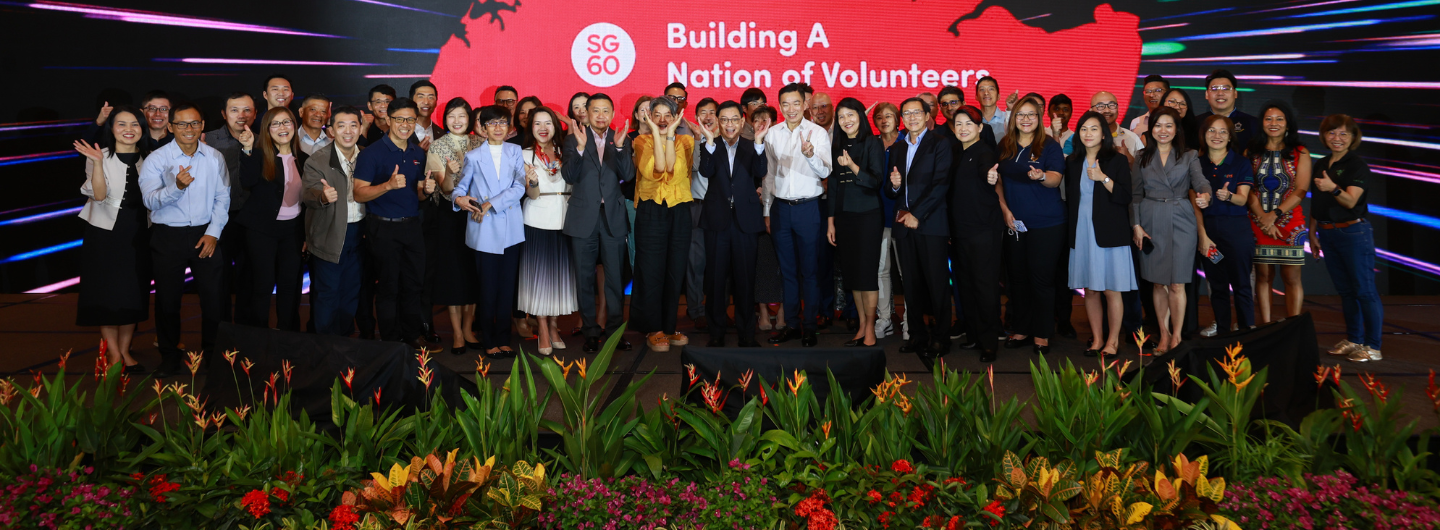 Group of people posed on stage in front of an SG60 "Building A Nation of Volunteers" backdrop.